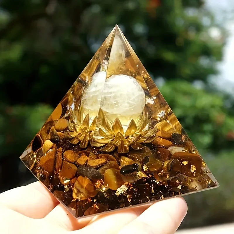 Pyramid-shaped crystal with a white sphere inside, held by a hand against a blurred natural background.