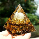 Pyramid-shaped crystal with a white sphere inside, held by a hand against a blurred natural background.