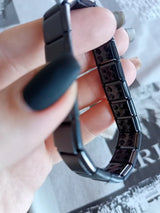Black metal bracelet held by a hand with a blurred background