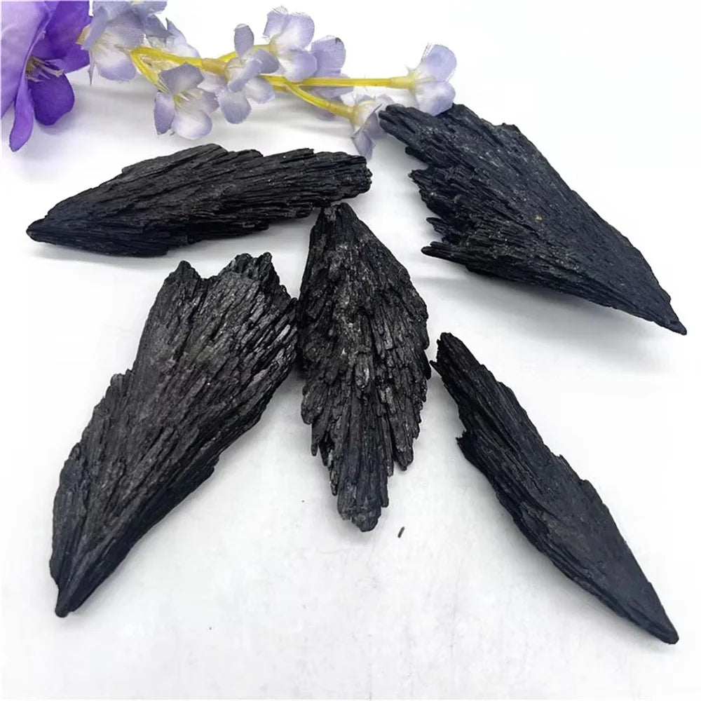 Black wing-shaped stones on a white surface with purple flowers in the background