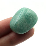 Green stone held between fingers on a white background