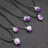 Necklaces with purple crystal pendants on black cords against a dark background