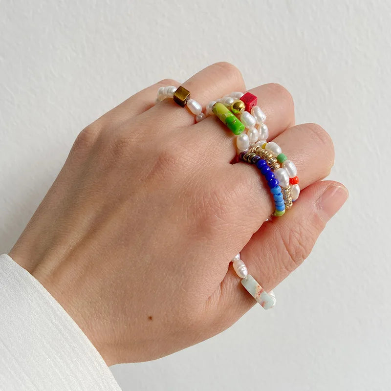 Hand wearing multiple colorful beaded rings on a plain background