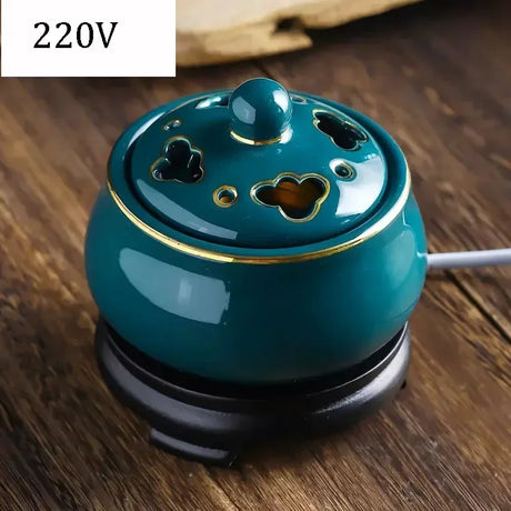 Teal ceramic oil burner on a wooden surface with '220V' label.