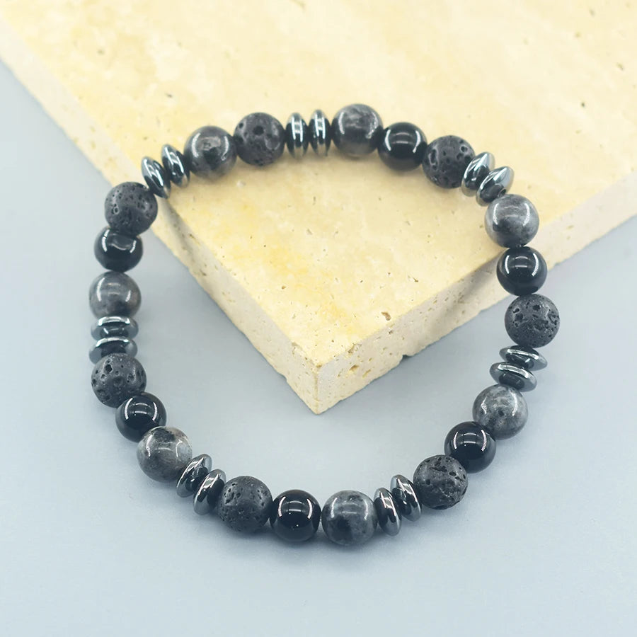 Black beaded bracelet on a light gray surface with a heart-shaped object in the background