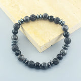 Black beaded bracelet on a light gray surface with a heart-shaped object in the background