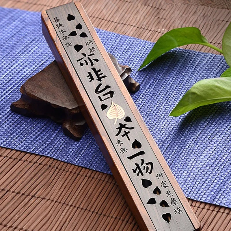 Wooden incense holder with engraved characters on a blue mat with green leaves.