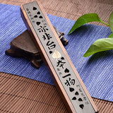 Wooden incense holder with engraved characters on a blue mat with green leaves.