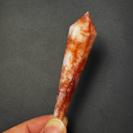 Hand holding a red and white crystal against a dark gray background
