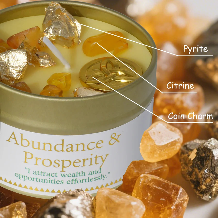 Candle labeled 'Abundance & Prosperity' with pyrite, citrine, and a coin charm.