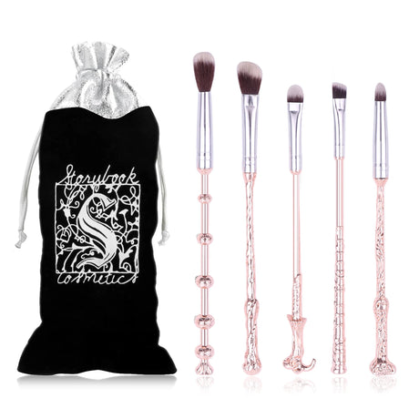 Set of makeup brushes with decorative handles next to a branded black drawstring bag on a white background