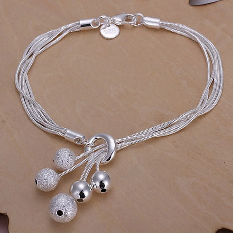 Silver bracelet with multiple strands and spherical charms on a beige background