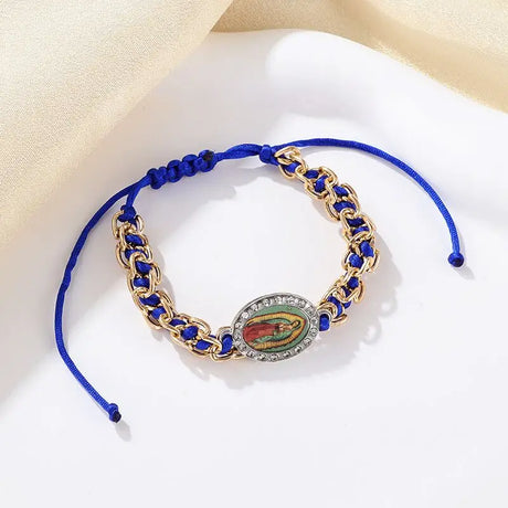 Bracelet with blue cord and gold chain featuring a religious emblem on a beige fabric background