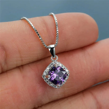 Silver necklace with a purple gemstone pendant held between fingers against a neutral background