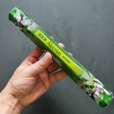 Hand holding a green Alecrim incense stick packaging against a dark background