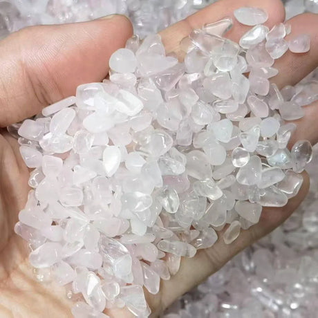 Hand holding small, clear to pink crystal chips against a blurred background