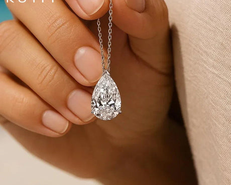 Teardrop-shaped diamond earring held by a hand with 'KUTPF' branding.