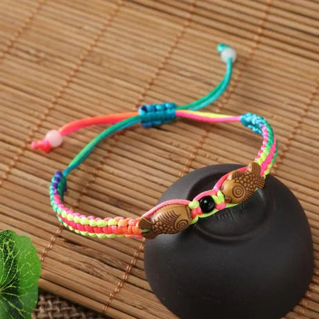 Colorful braided bracelet with fish charm on a black stone and bamboo mat background