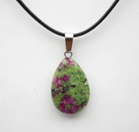 Teardrop-shaped pendant with green and pink speckled stone on a black cord against a white background