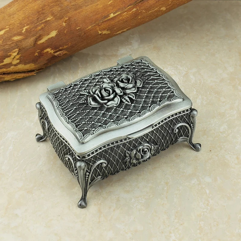 Decorative silver jewelry box with rose design on a beige surface