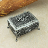 Decorative silver jewelry box with rose design on a beige surface