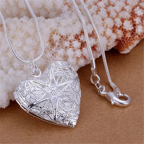 Silver heart-shaped locket with starfish design on a beige surface with coral background