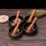 Set of four bronze singing bowls with wooden mallets on a wooden surface.