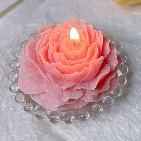 Pink rose-shaped candle with a lit wick on a white textured surface