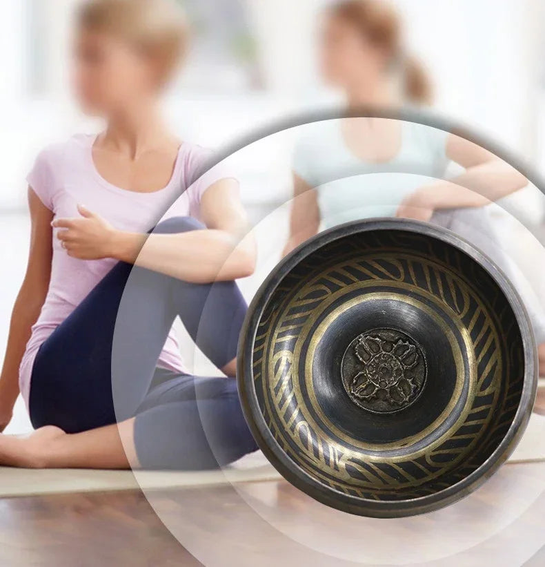 Close-up of a decorative metal bowl with intricate designs, blurred background of people sitting on the floor.