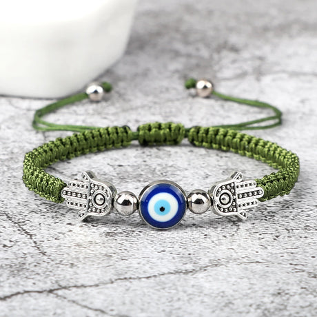 Green braided bracelet with Hamsa hand and evil eye charm on a gray surface