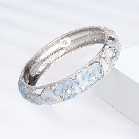 Silver bracelet with blue floral designs on a light gray background