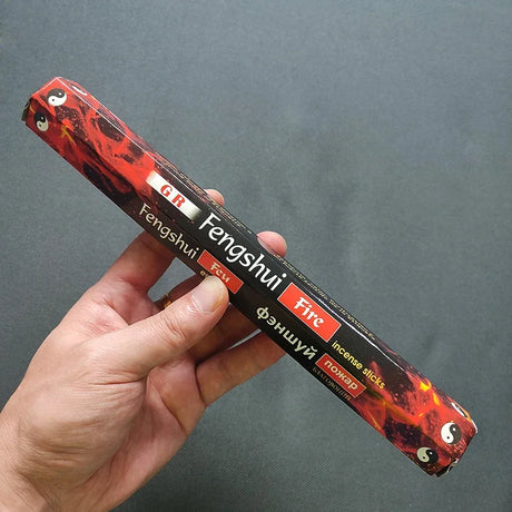 Hand holding a pack of Fengshui Fire incense sticks against a gray background