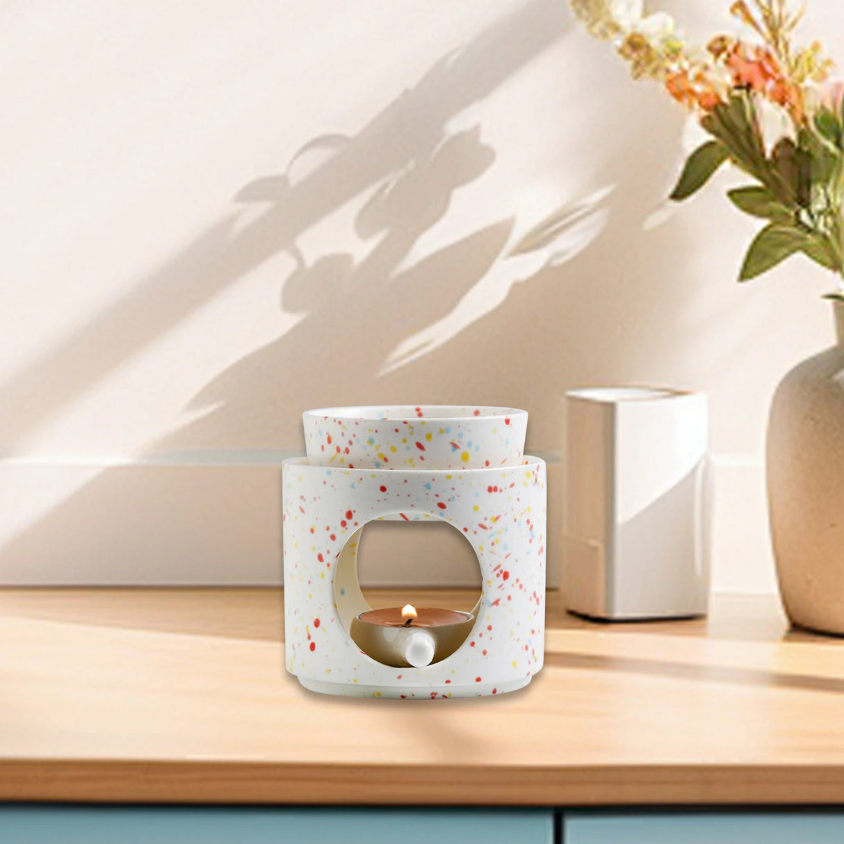 Speckled ceramic candle holder on a wooden surface with a vase of flowers in the background