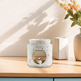 Speckled ceramic candle holder on a wooden surface with a vase of flowers in the background