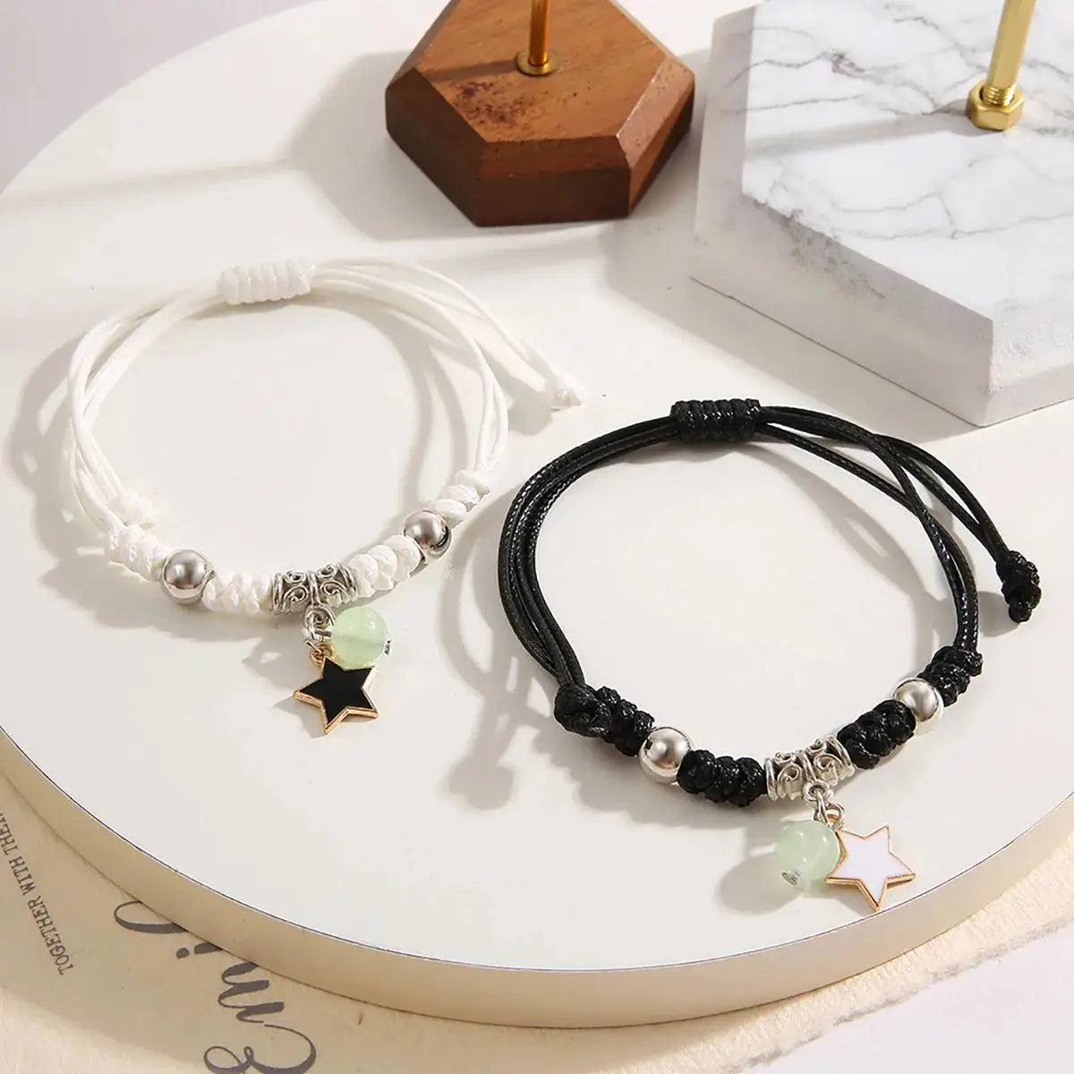 Two bracelets, one white and one black, with star charms on a marble surface.