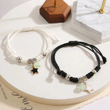 Two bracelets, one white and one black, with star charms on a marble surface.
