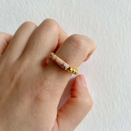 Gold beaded ring on a person's finger against a plain background