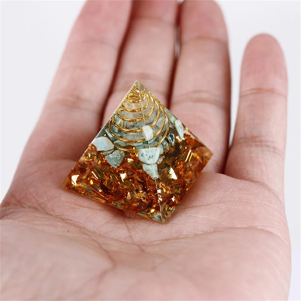 Pyramid-shaped crystal with gold and green elements held in a hand against a white background