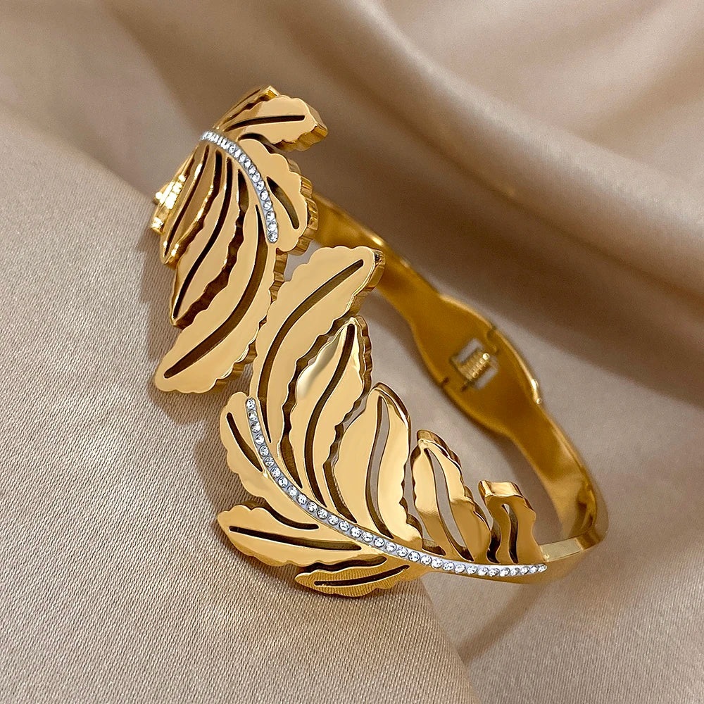Gold bracelet with leaf design and embedded stones on a beige fabric background