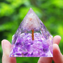 Pyramid-shaped crystal with purple and white stones held by a hand against a green blurred background
