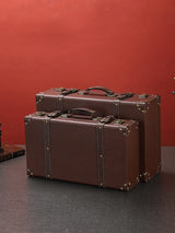 Two brown suitcases on a dark surface with a red background