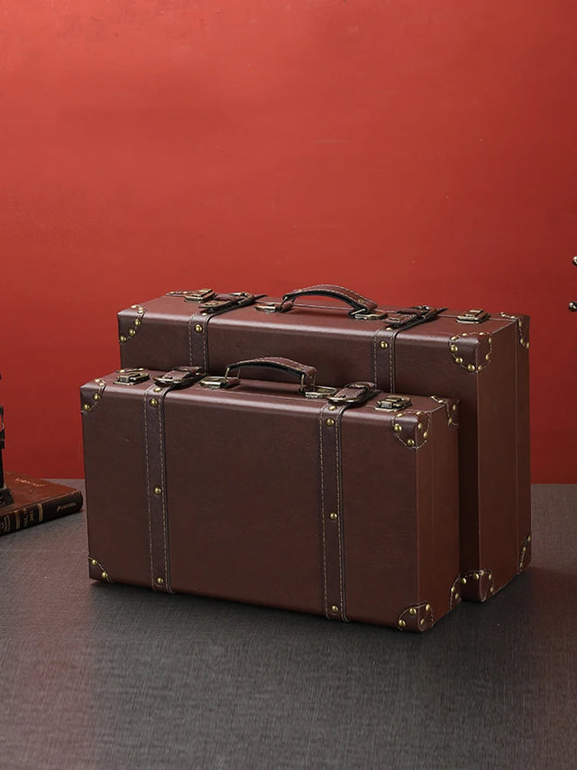 Two brown suitcases on a dark surface with a red background