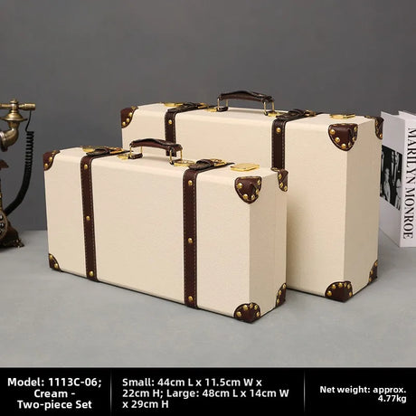 Two cream-colored suitcases with brown straps on a gray surface.