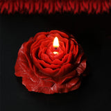 Red rose-shaped candle with a lit wick on a black background