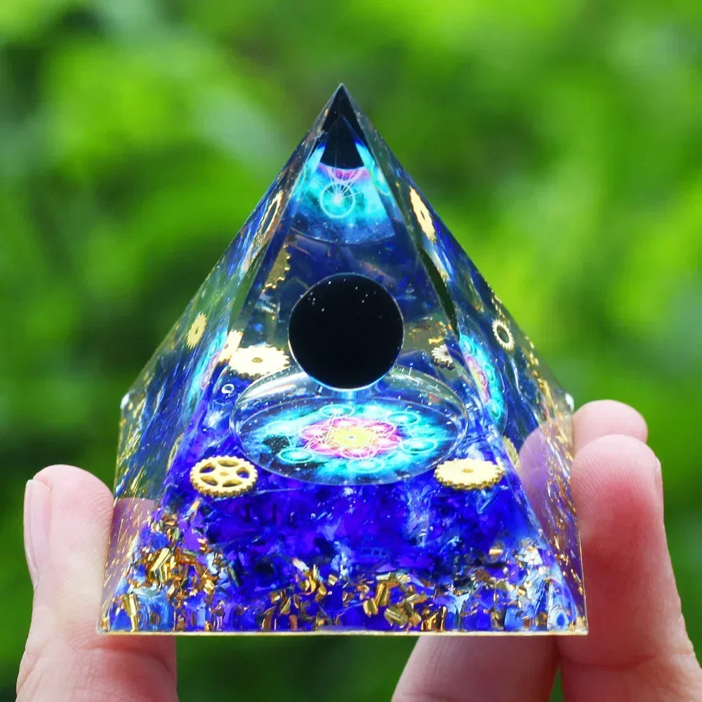 Blue pyramid-shaped crystal with intricate designs held in a hand against a green blurred background