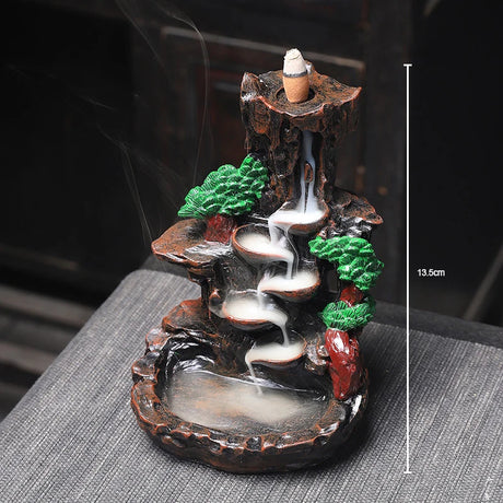 Decorative incense burner with a mountain and tree design on a gray surface.