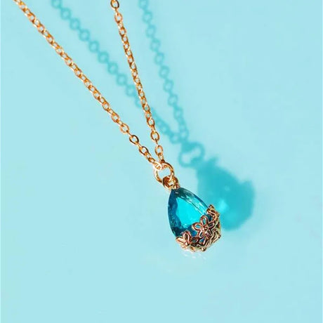 Gold necklace with a blue teardrop pendant on a light blue background