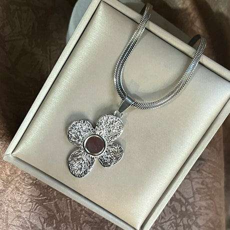 Silver necklace with a flower pendant on a light gray box