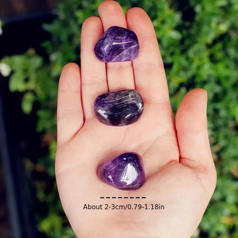 Three purple crystals held in a hand with a green leafy background