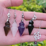 Four crystal pendulums on chains held in a hand with a blurred green background